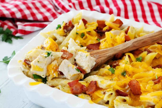 A casserole dish full of pasta with cubes of chicken, bacon, and cheese.