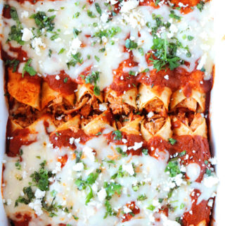 A casserole dish lined with Crock Pot Enchiladas topped with cheese and a Ranchero Style Sauce.