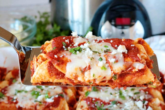 Enchiladas on a spatula in front of a slow cooker.