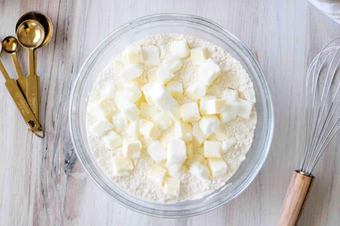 A bowl of dry ingredients with butter and shortening cubes on top them.