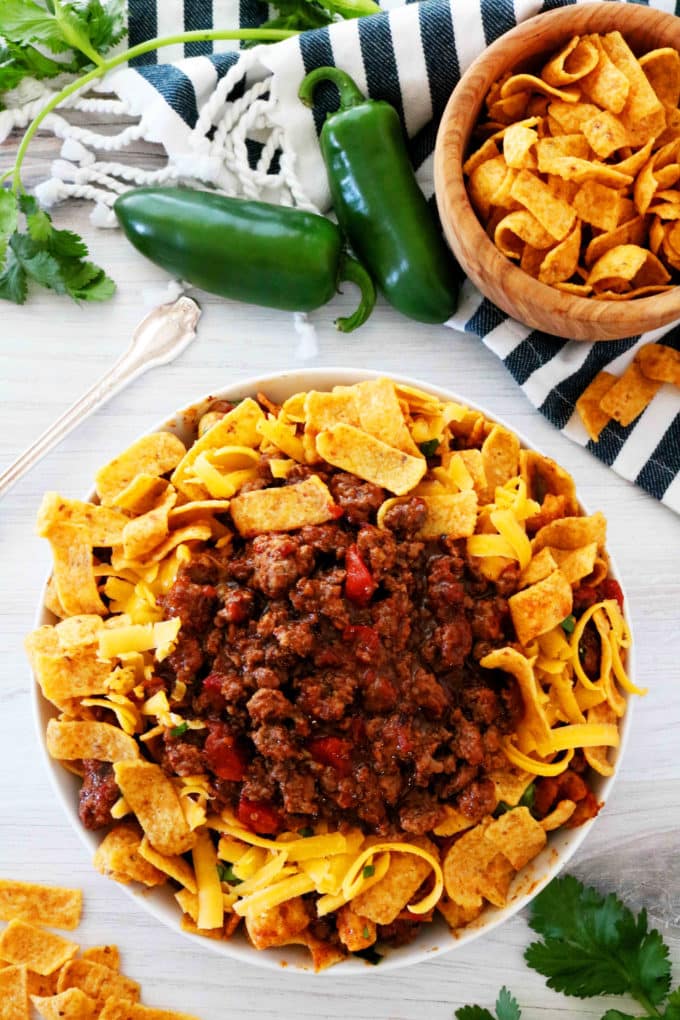 An overhead shot of Frito pie with a bowl of fritos and a fork off to the side.