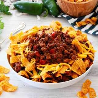 Frito Pie in a bowl surrounded by chips and jalapenos.