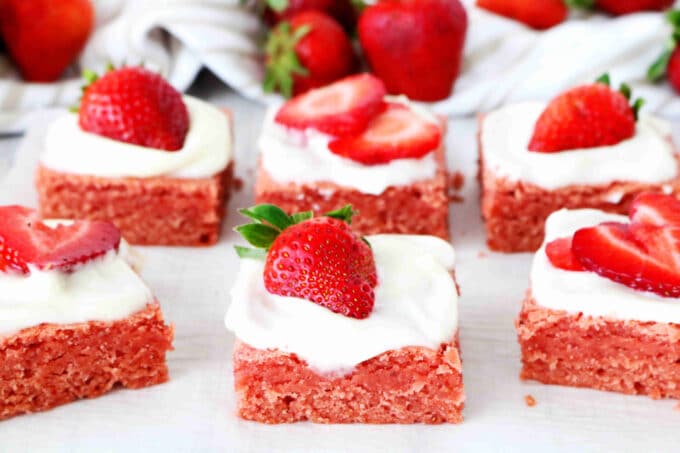 Strawberry brownies topped with icing and halved strawberries. 