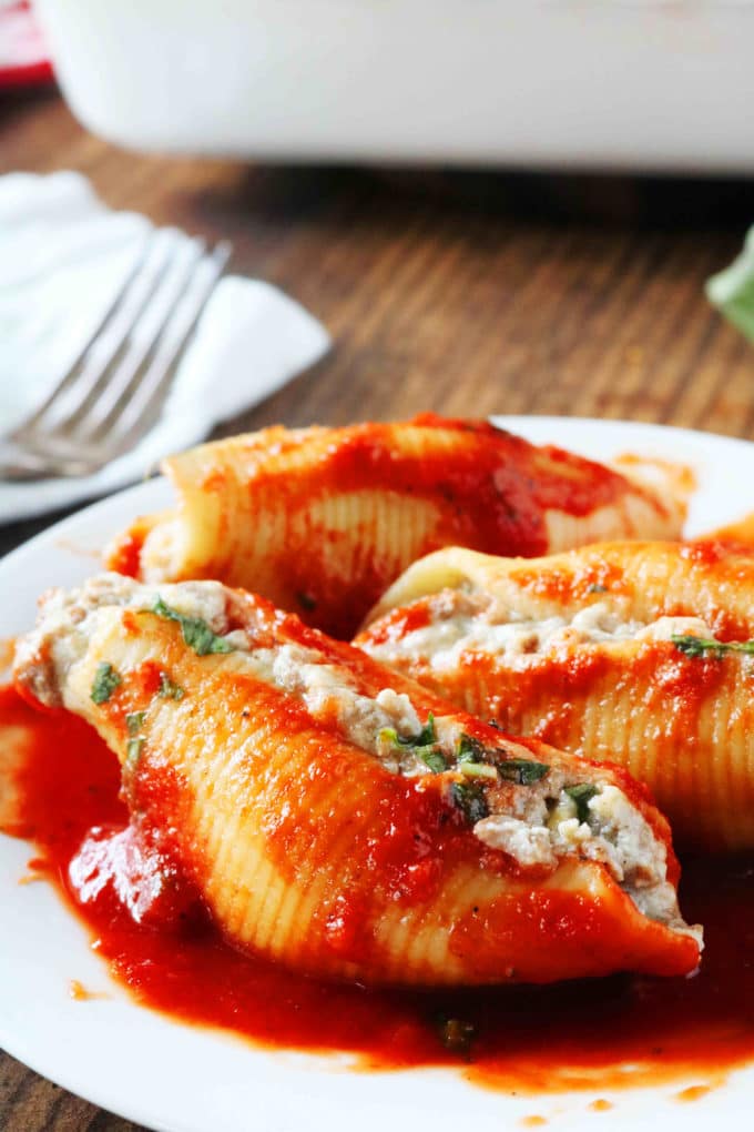 A plate of stuffed shells with a casserole dish and fork in the background.