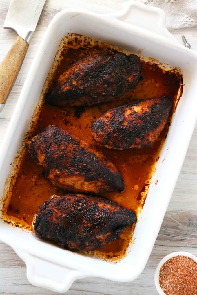 An overhead shot of blackened chicken breasts in a casserole dish.