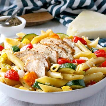 Sliced chicken sitting on top of pasta primavera in a bowl.