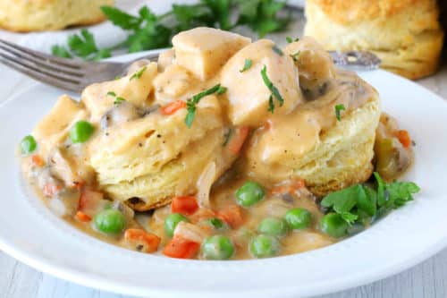 Chicken a la king poured over biscuits with extra biscuits in the background.