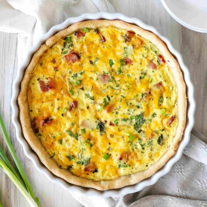 An overhead shot of Quiche Lorraine baked in a quiche dish with a scatter or green onions around it.