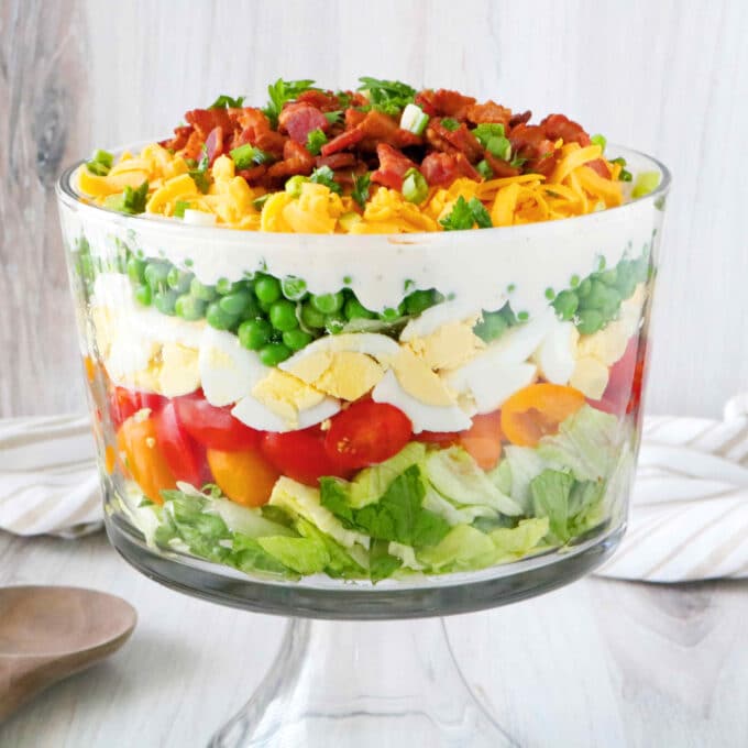 7-Layer Salad in trifle bowl with a serving spoon next to it and a towel laying behind the dish.