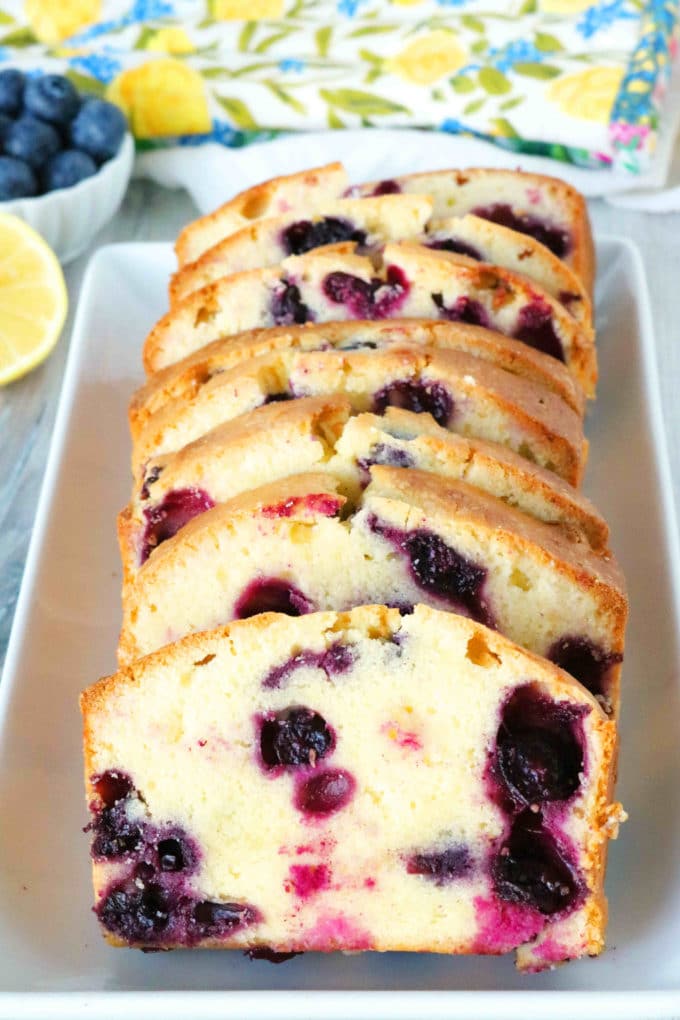 Slices of blueberry pound cake on a platter with lemon and blueberries in the background.