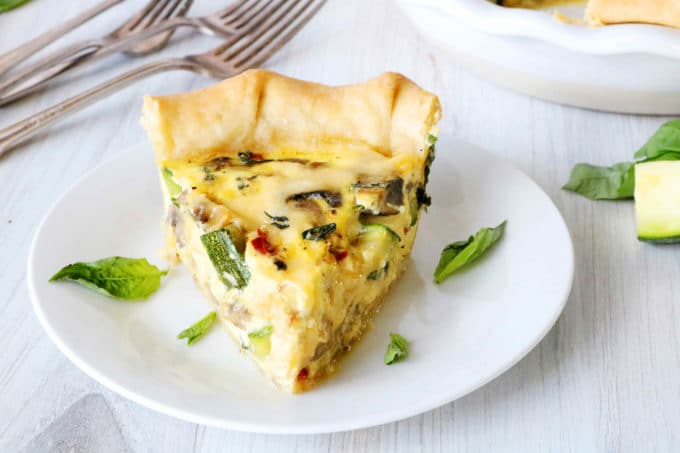 A slice of veggie quiche on a plate with forks behind it.