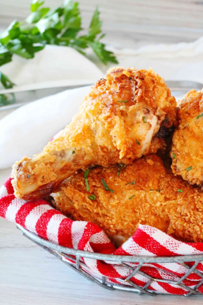 A close up shot of a fried chicken leg in a basket on top of other pieces of fried chicken.