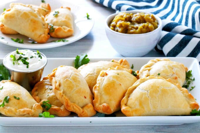 A platter of empanadas with a bowl of green chiles behind it.