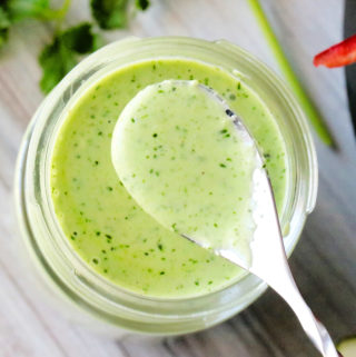 A spoon being held over a bottle of cilantro lime dressing.