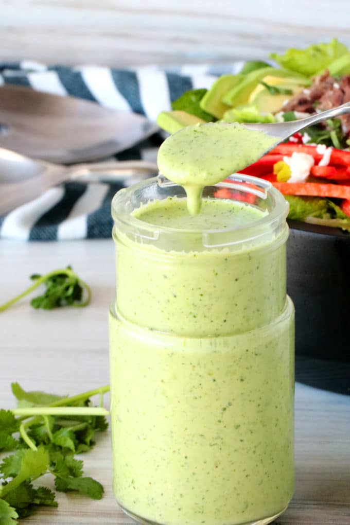 A spoon over a bottle of cilantro lime dressing with dressing dripping off of it.