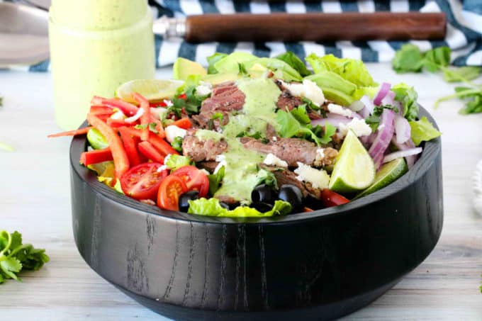 Fajita salad in a bowl with limes, beef, peppers, and dressing.