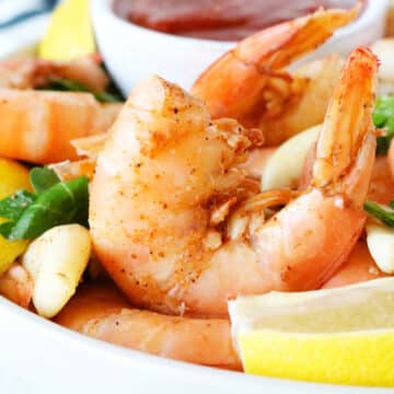 A close up shot of steamed shrimp in a bowl surrounded by lemon wedges.