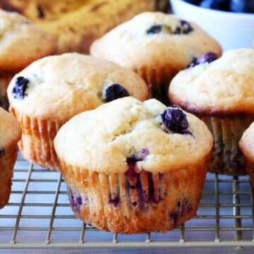 Blueberry Banana Muffins on a cooling rack with a bowl of blueberries behind them.