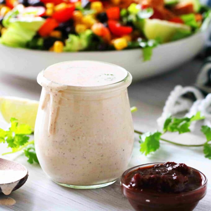 A jar of Chipotle Ranch Dressing with cilantro, chipotle peppers, and limes around it.
