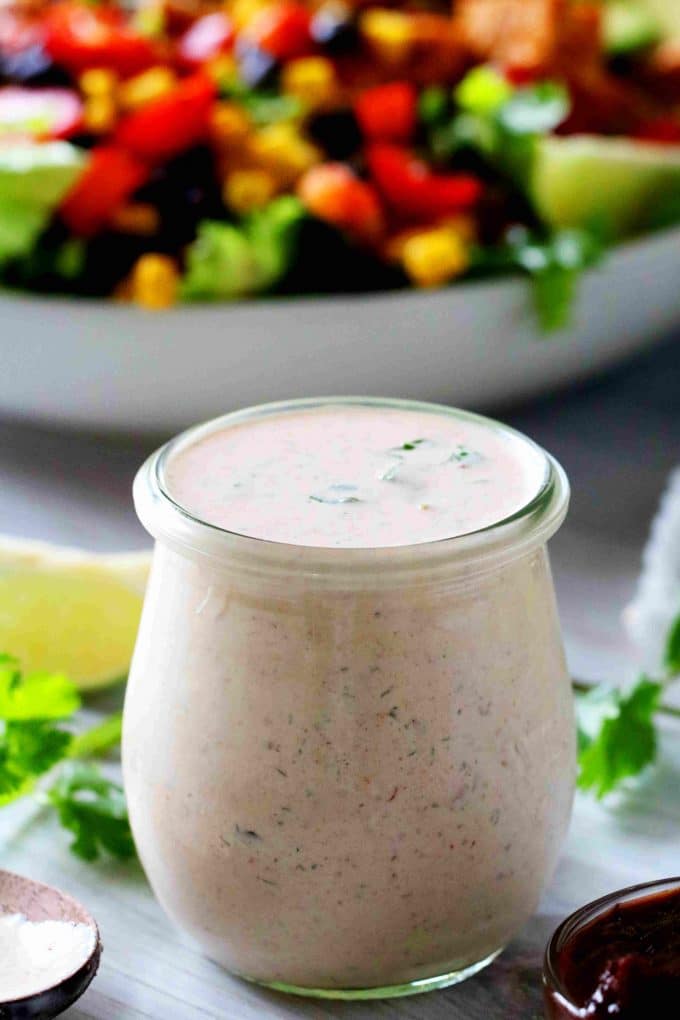 A jar of chipotle ranch dressing with a bowl of salad in the background.