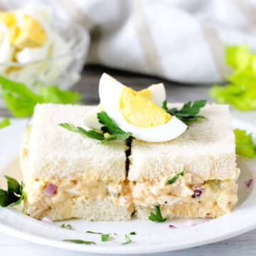 Tuna Egg Salad Sandwiches on a white plate with chopped eggs in the background.
