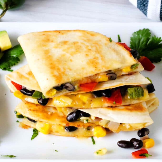 Veggie Quesadillas with corn, black beans, and peppers stacked on a white serving platter surrounded by scattered beans and corn.