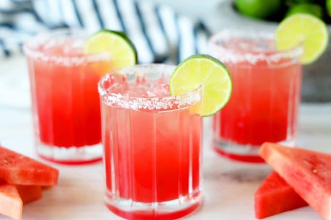 Watermelon Margaritas with a lime garnish and a salted rim and wedges of watermelon surrounded the glasses. 