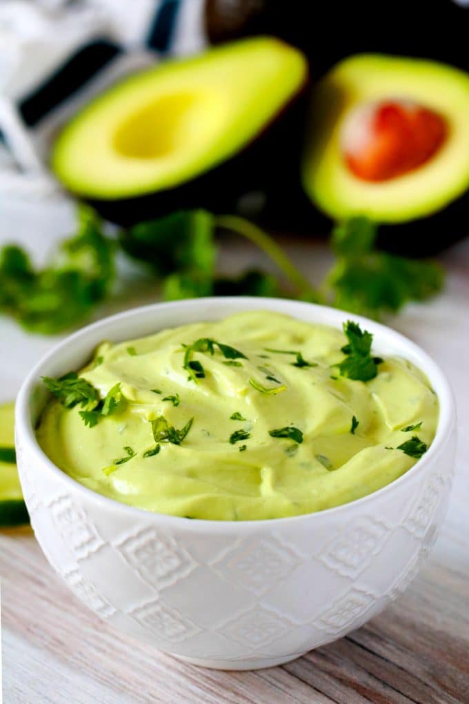 A close up shot of avocado crema with a cilantro garnish and avocados in the background.