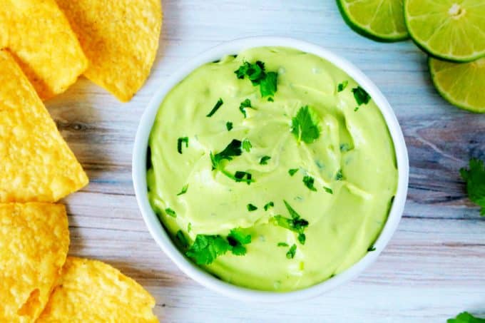 An overhead shot of avocado crema with chips and limes surrounding it.