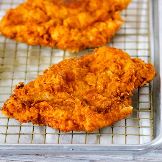 A close up shot of chicken fried chicken on a cooling rack over paper towels.