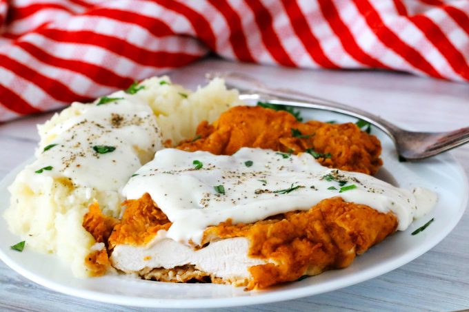 Chicken fried chicken on a plate with a slice cut out of it.