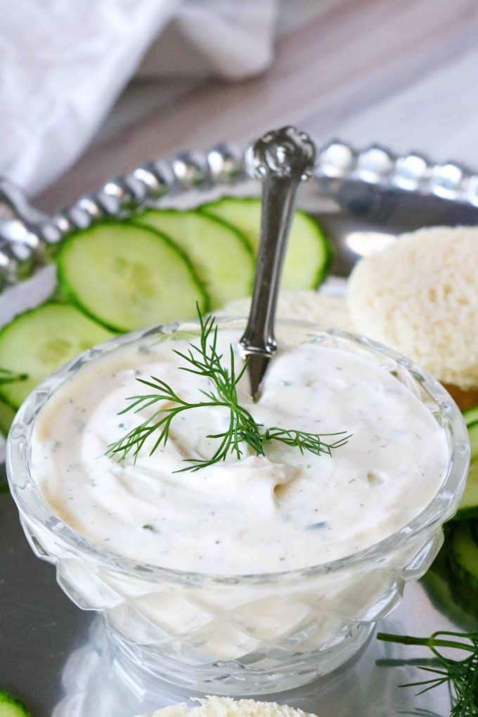 Dill sauce in a glass bowl with a sprig of dill on top of it.