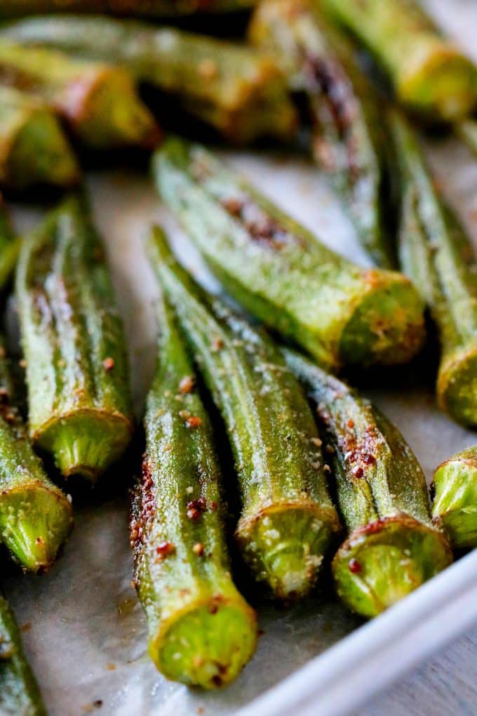 A close up shot of roasted okra in a rimmed sheet pan.