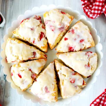 An overhead shot of 8 strawberry scones with glaze in a circular pattern on a cake stand.