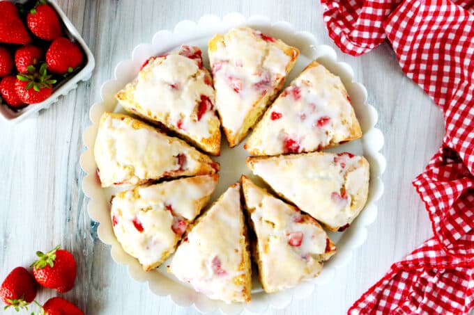 An overhead shot of 8 strawberry scones with glaze in a circular pattern on a cake stand.