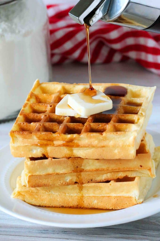 A stack of waffles with syrup being drizzled over them.