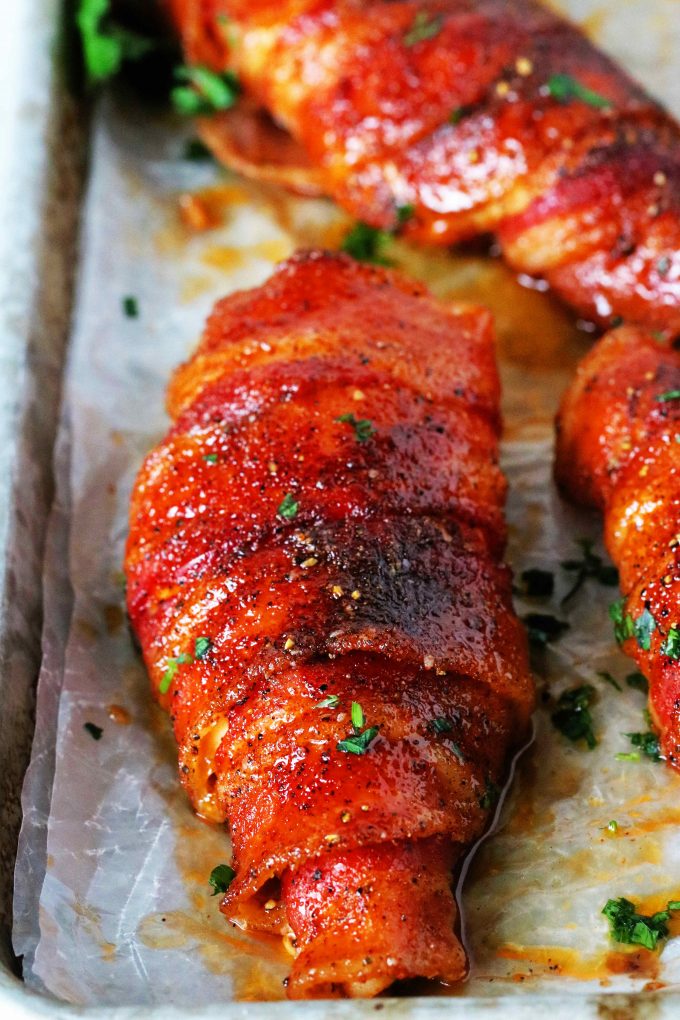 A close up shot of bacon wrapped chicken on a foil lined pan.