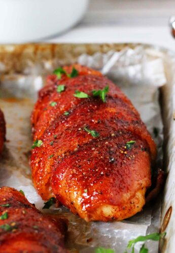 A close up shot of bacon wrapped chicken on a foil lined pan.