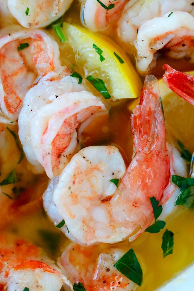 A close up shot of shrimp in a butter sauce with a lemon wedge next to it. 