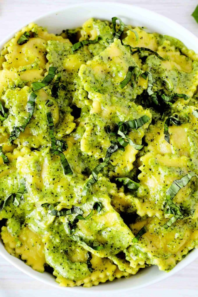 An overhead shot of ravioli tossed with cream pesto sauce in a white bowl.