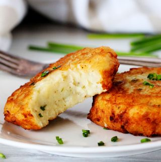 Two potato patties on a plate with chives scattered around them.