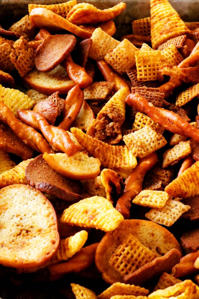 A close up shot of Different types of Chex cereal, pretzels, bagel chips, bugels, and rye chips on a sheet pan. 