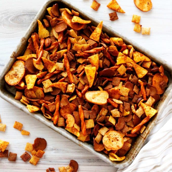 Spicy Chex Mix on a sheet pan with scatters of chex cereal and bugels around it.