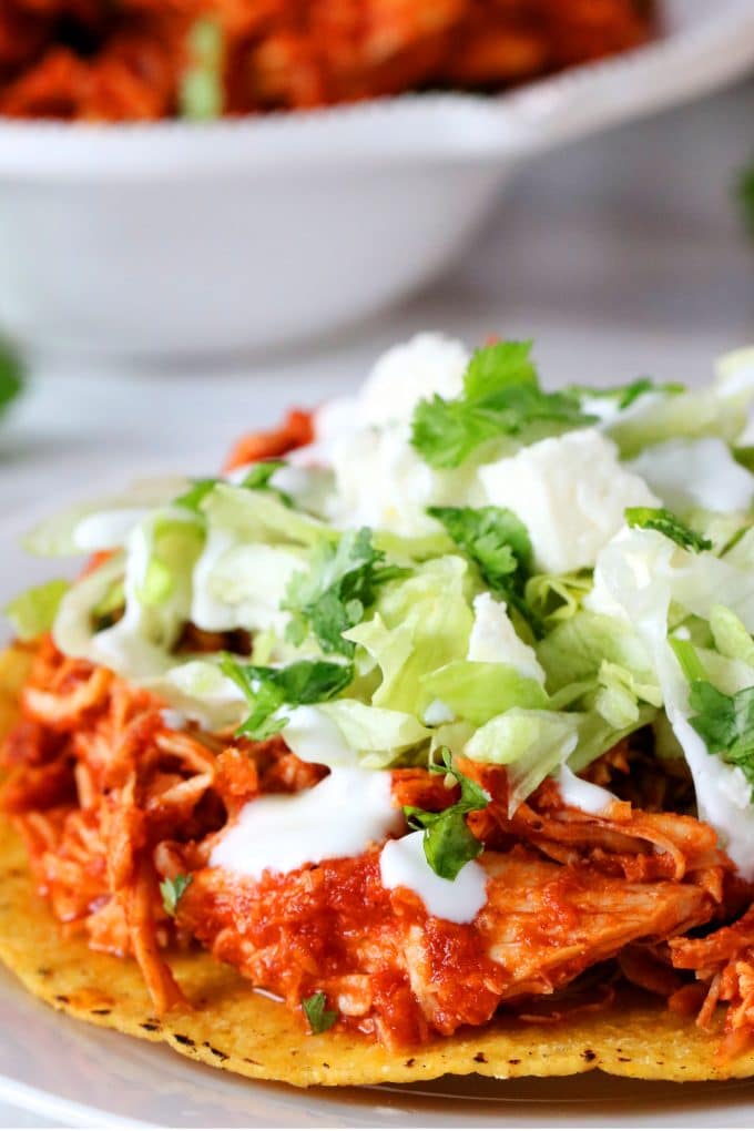 A close up shot of a tostada topped with chicken tinga and lettuce.