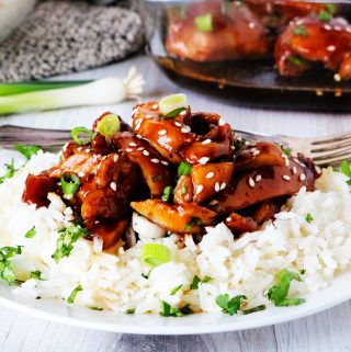 Baked Teriyaki Chicken over white rice on a plate with a casserole dish in the background.