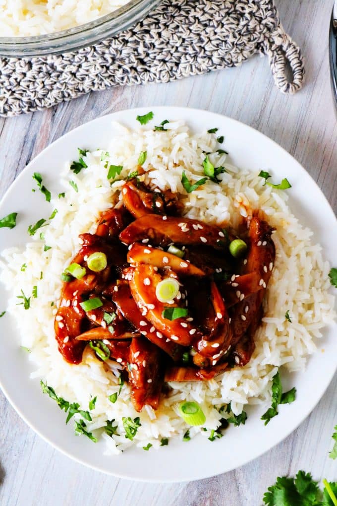 An overhead shot of sliced teriyaki chicken over white rice garnished with sesame seeds and green onions.