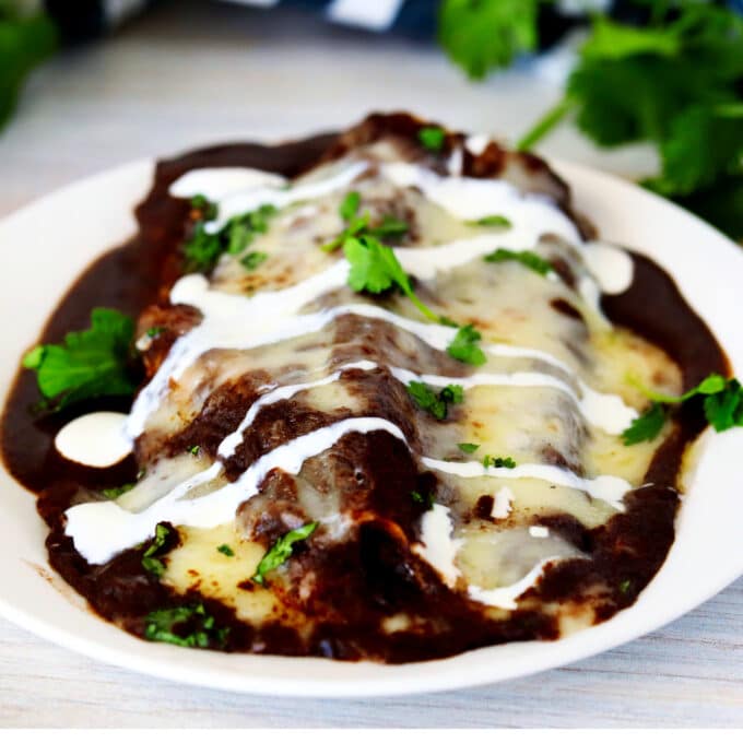 Enfrijoladas on a plate topped with a drizzle of sour cream.