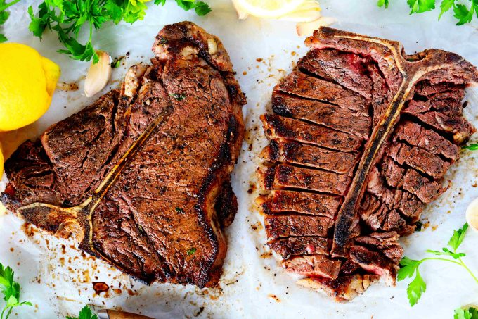 Two porterhouse steaks surrounded by parsley and lemon. 