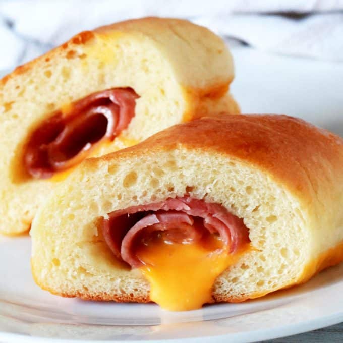 A ham and cheese kolache cut in half with cheese oozing out on a plate.