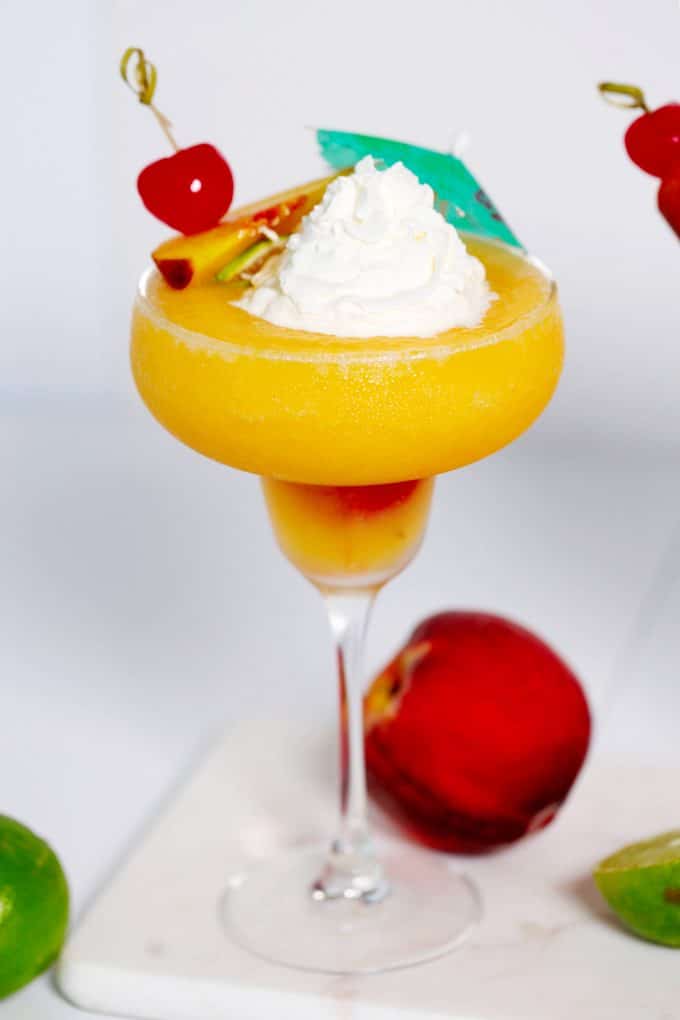 Peach daiquiri in a margarita glass topped with fruited skewer, whipped cream, and a cocktail umbrella.